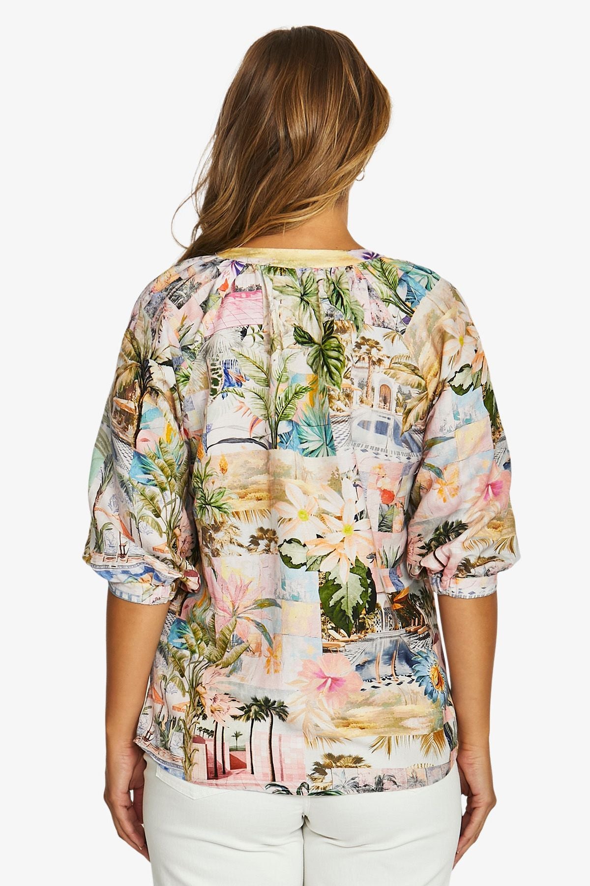  back  view wearing a short sleeve top with a colorful tropical and beach themed print, paired with white pants.