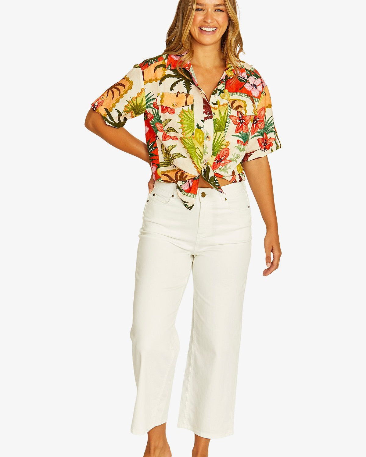 Front View short sleeve button up shirt with a colorful tropical floral print, paired with white cropped pants and beige slide sandals.