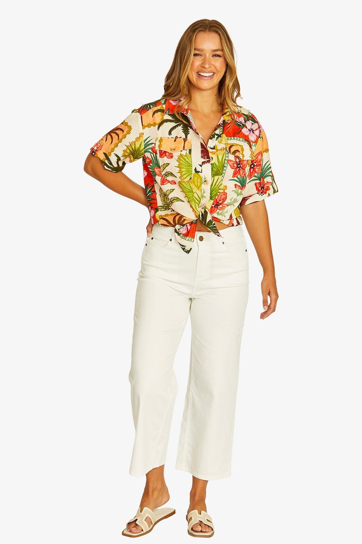 Front View short sleeve button up shirt with a colorful tropical floral print, paired with white cropped pants and beige slide sandals.