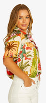 Side View short sleeve button up shirt with a colorful tropical floral print, paired with white cropped pants .