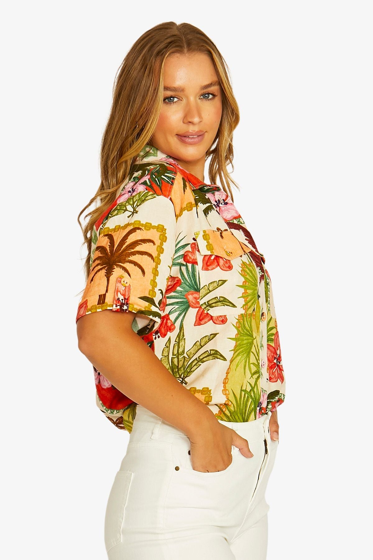 Side View short sleeve button up shirt with a colorful tropical floral print, paired with white cropped pants .