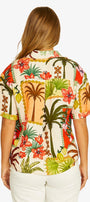 Back view short sleeve button up shirt with a colorful tropical floral print, paired with white cropped pants and beige slide sandals.