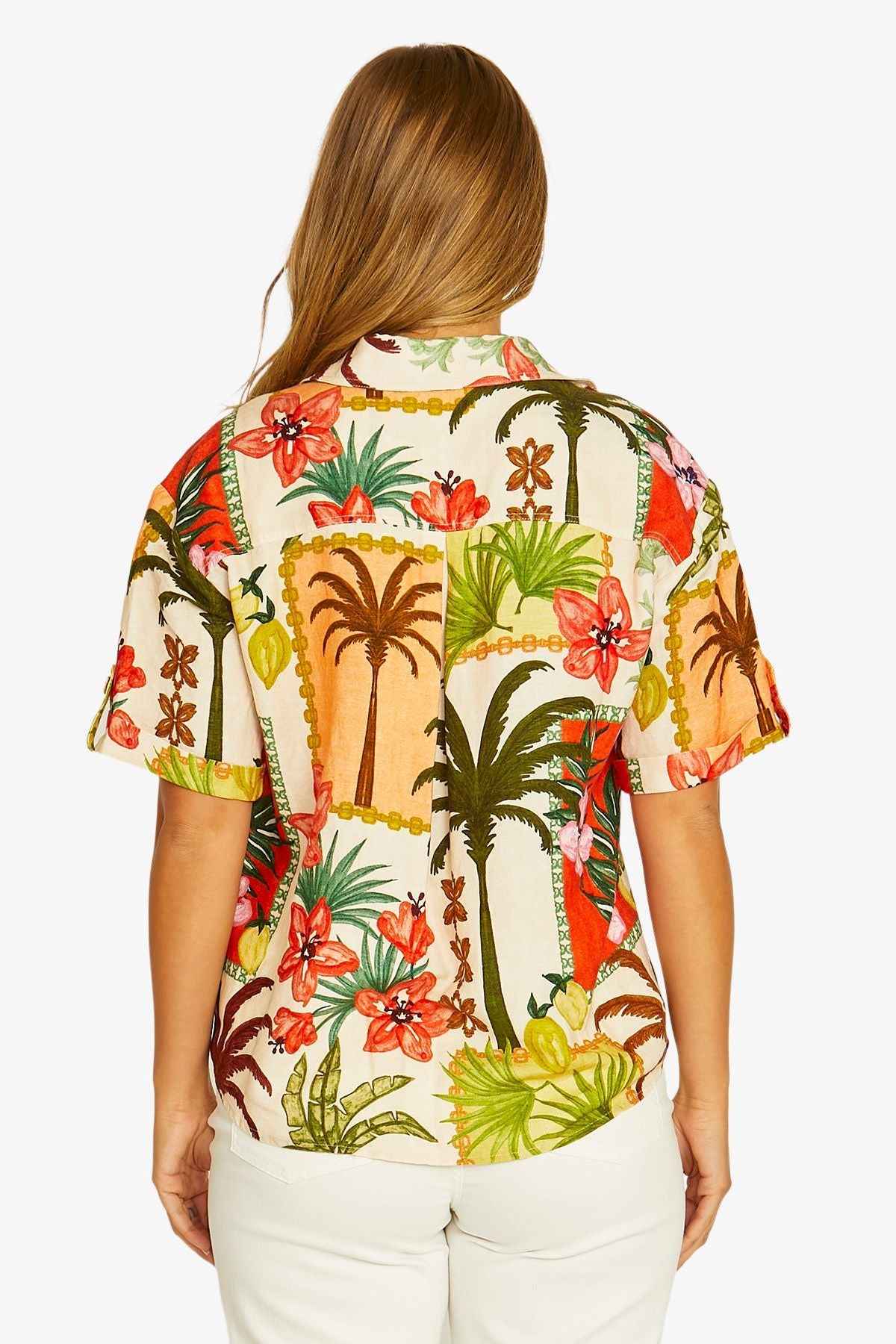 Back view short sleeve button up shirt with a colorful tropical floral print, paired with white cropped pants and beige slide sandals.