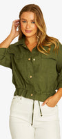 A woman modeling an olive green cropped button-up shirt with chest pockets and white drawstring pants against a light gray studio background.