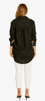 A woman viewed from the back wearing a black long-sleeve button-up shirt with side pockets, white cropped pants, and black heels, against a plain white background.