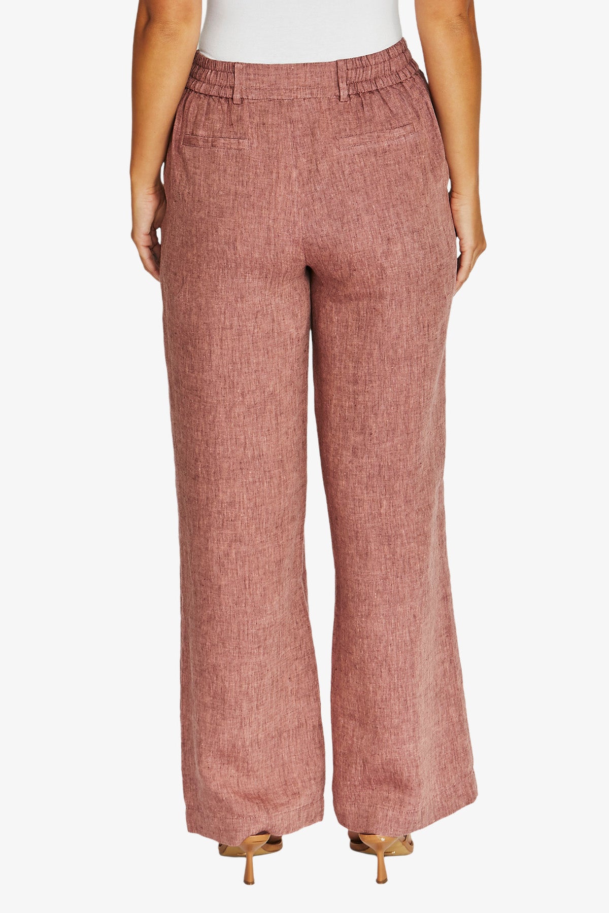 Back View waist down wearing dusty rose wide leg trousers with a textured linen like fabric, paired with a white top and beige heels.