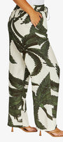 A person wearing high-waisted wide-leg pants with a bold green palm leaf print on an off-white background, paired with tan heeled sandals against a light gray studio background.