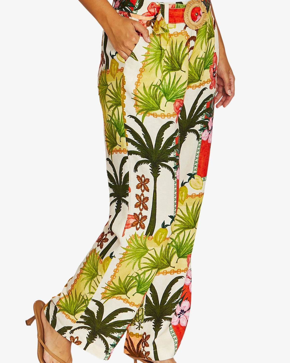 Side View high waisted, wide leg tropical print pants with a white top and tan heeled sandals, shown against a plain light gray studio background.
