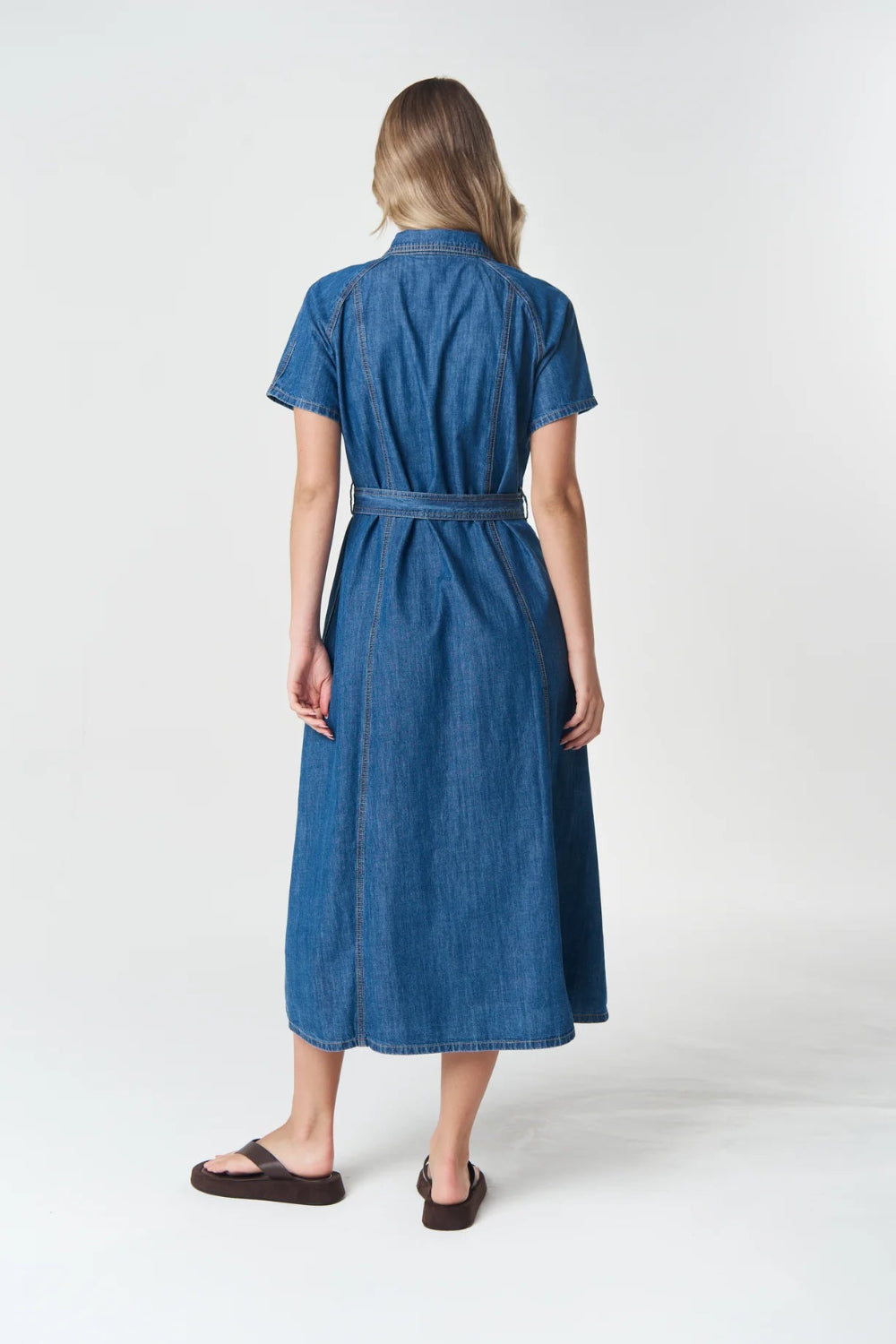 Back View  a blue denim midi dress with short sleeves and a matching waist tie, paired with dark brown sandals.