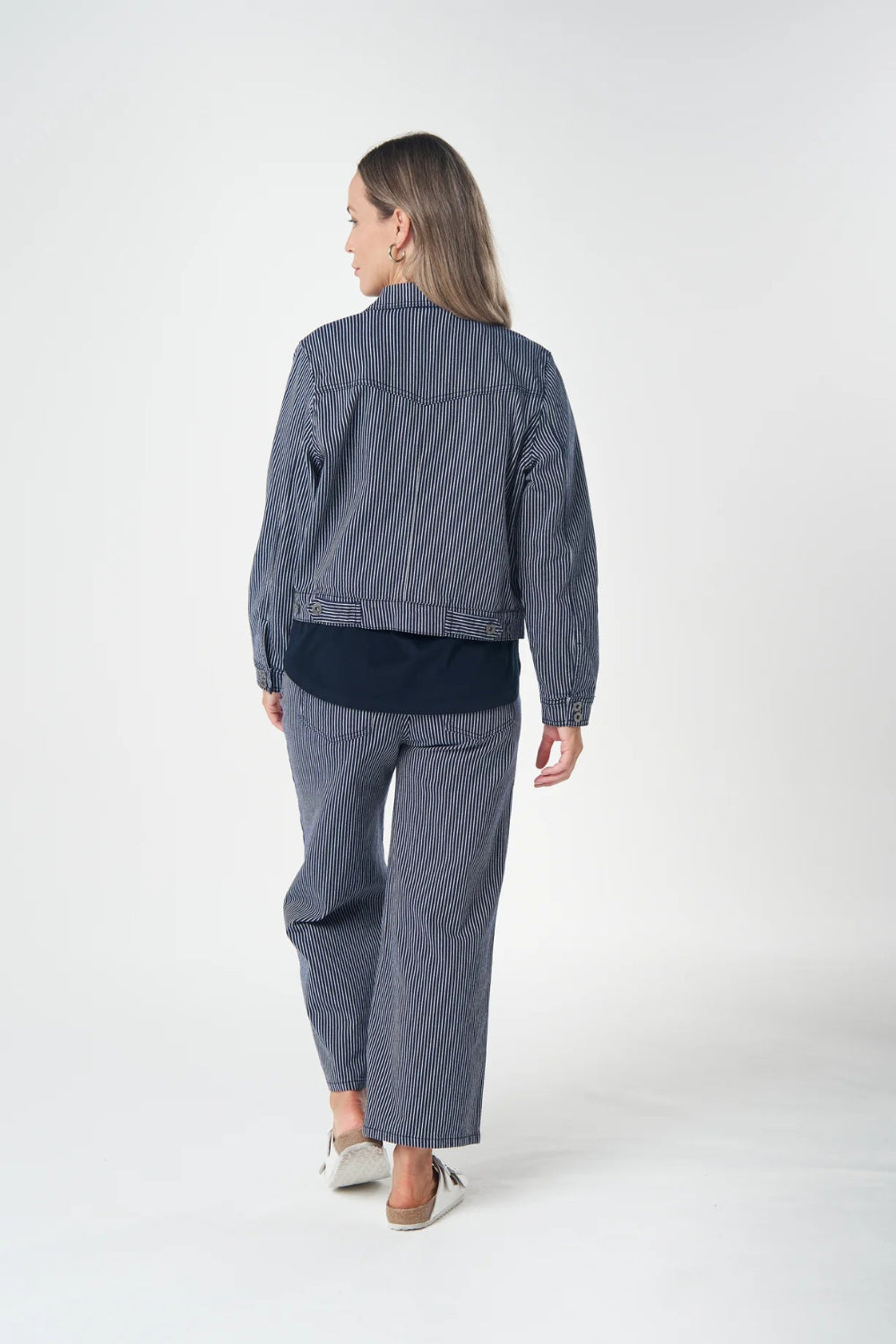 Back view matching navy blue denim jacket and wide leg pants set, styled with a dark navy t-shirt and white slip on shoes.