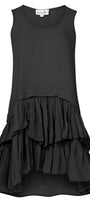 longline silhouette top with a scoop neckline and a gathered, layered peplum hem, standing by a body of water with a blue sky in the background.