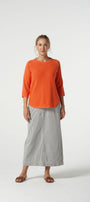 Woman wearing an orange top and gray skirt on a white background