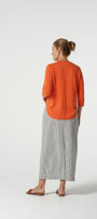 Woman wearing an orange sweater and gray pants on a white background