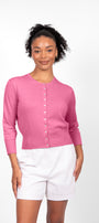 A woman wearing a pink cropped 3/4 sleeve cardigan with white shorts.