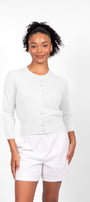 A woman wearing a white cropped 3/4 sleeve cardigan with white shorts.