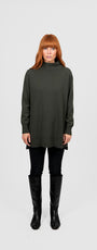 Woman wearing a long dark green turtleneck sweater and black pants .