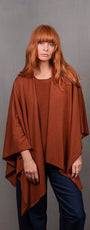 Woman wearing a brown poncho over a red top and blue jeans .