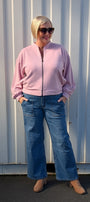 Front view a light pink zip up jacket, blue wide leg jeans, and tan boots front view.