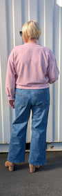 Back view  a light pink long sleeve top and wide leg blue jeans.
