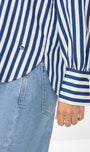 Close up of a person wearing a blue and white striped shirt with rolled up sleeves and light blue jeans.