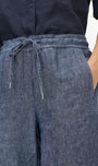 Close-up of a person wearing wide-leg blue linen pants with an elastic drawstring waist and side pockets, paired with a dark navy top against a plain white background.