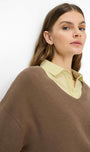 A woman wearing a brown ribbed knit sweater layered over a pale yellow collared shirt, photographed against a plain white background.