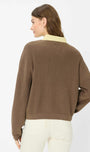 A woman shown from the back wearing a brown ribbed knit sweater with a light beige collar, paired with off-white pants, against a plain white studio background.