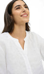 A woman wearing a white linen button-up shirt, shown from the chest up against a clean white background.