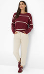 Woman wearing a burgundy sweater with white stripes and cream pants.