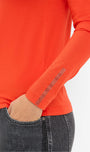 Close up of a person wearing an orange long sleeve top with rhinestone details on the cuffs .