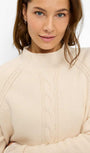 Woman wearing a beige sweater against a white background