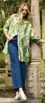 Woman in a floral shirt and blue jeans standing in a garden setting.