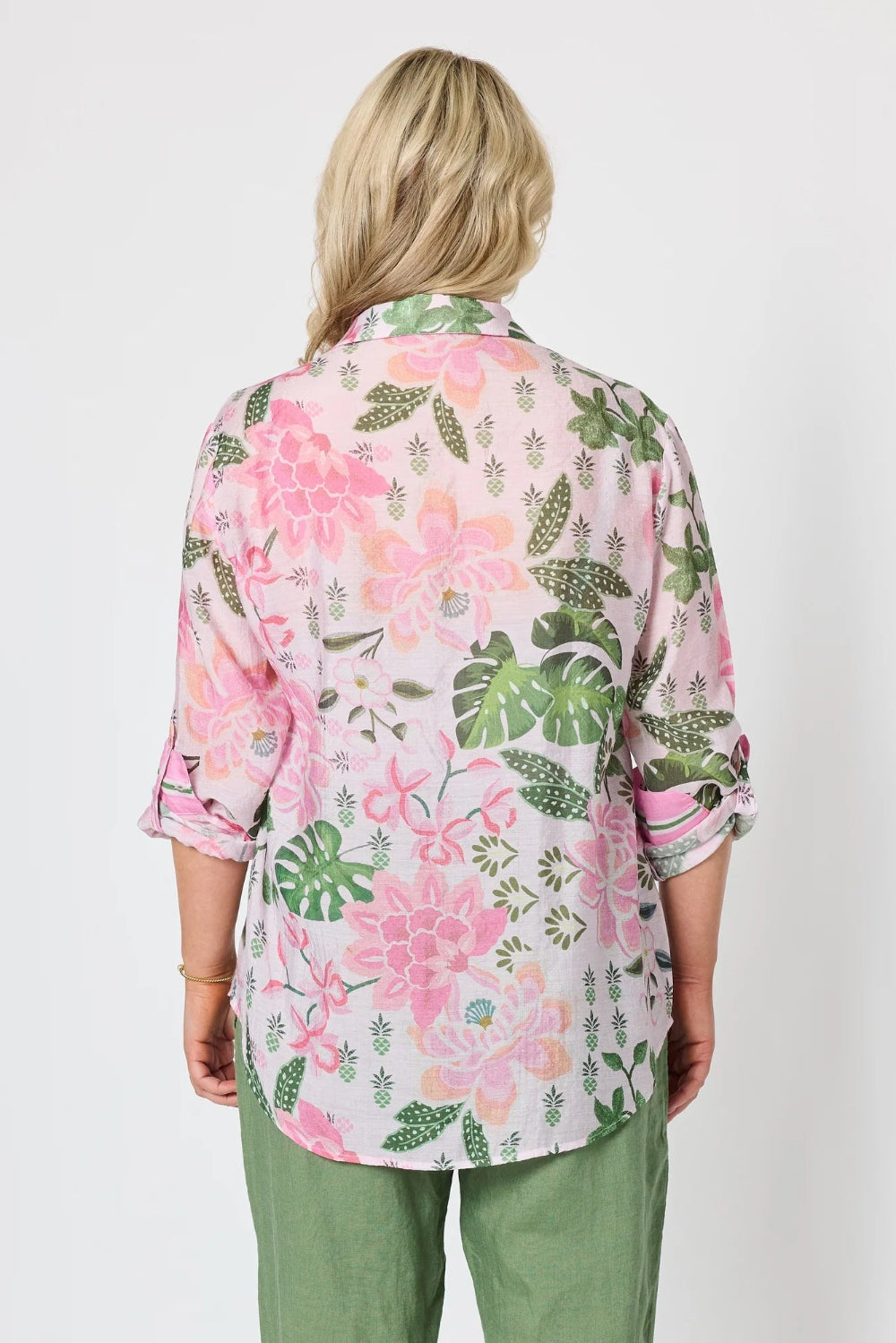 A woman viewed from the back wearing a light pink floral button up shirt with green and pink botanical print, paired with sage green pants,.