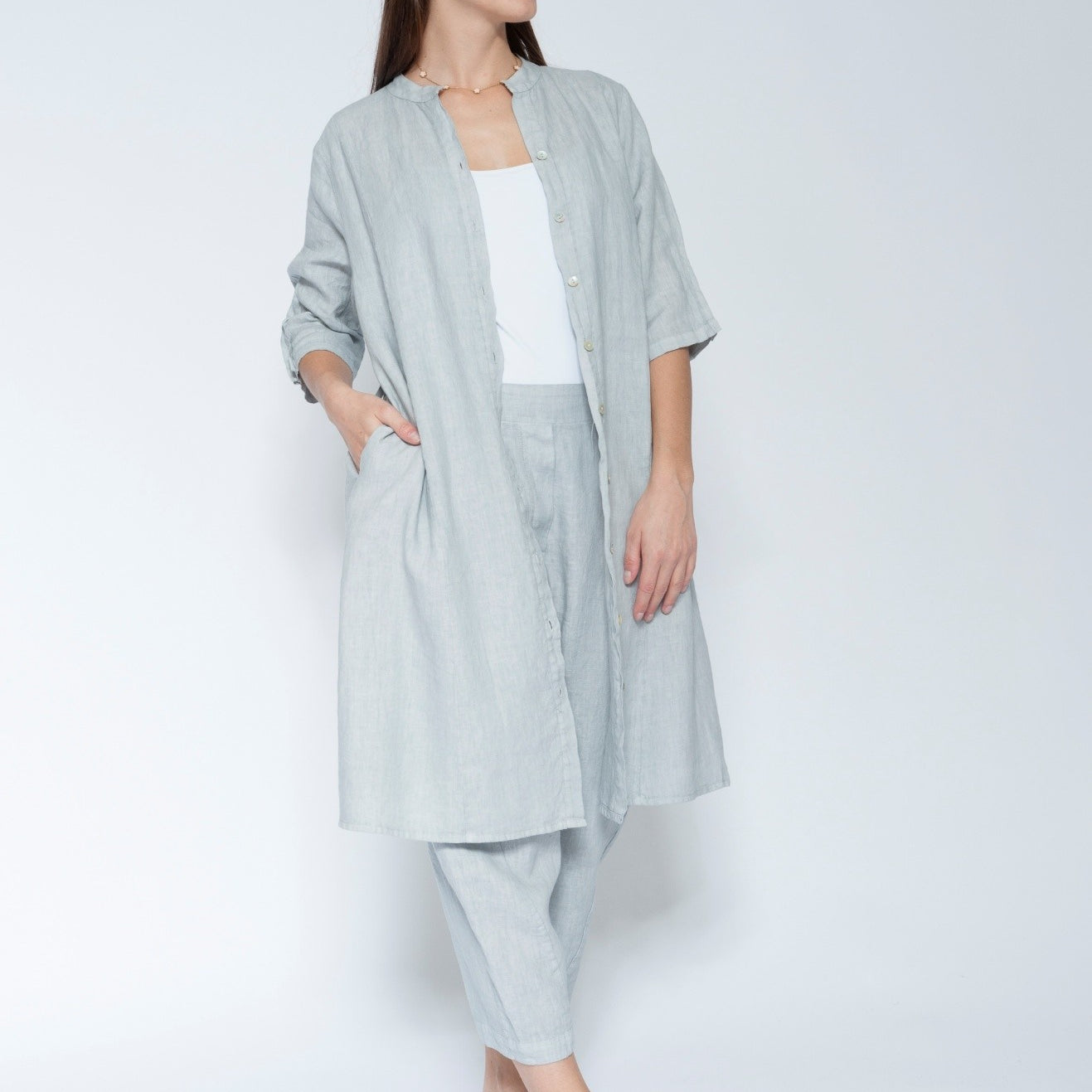 Front view light blue grey linen long shirt dress with matching trousers, worn over a white tank top and black slide sandals.