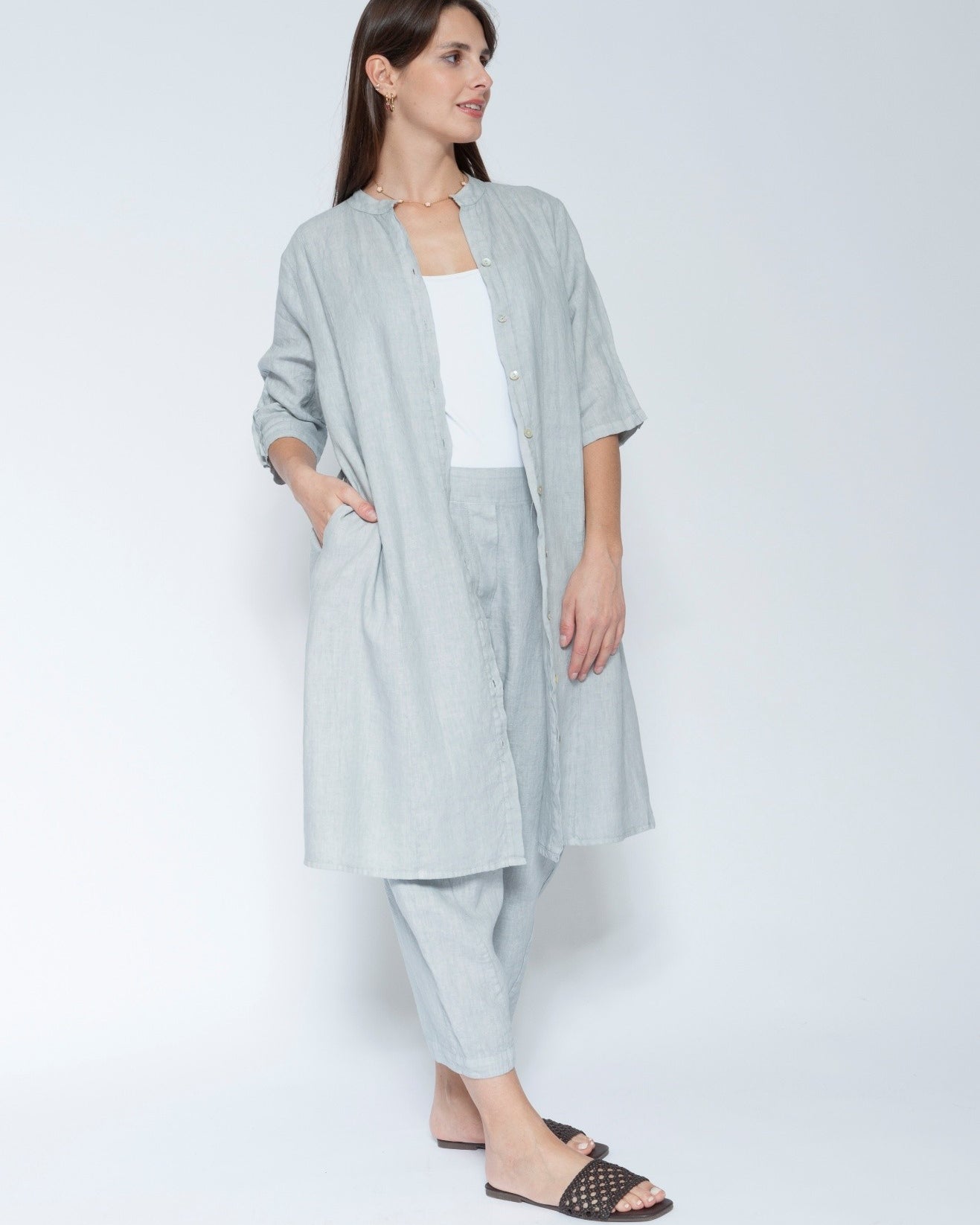 Front view light blue grey linen long shirt dress with matching trousers, worn over a white tank top and black slide sandals.