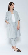 Front view light blue grey linen long shirt dress with matching trousers, worn over a white tank top and black slide sandals.
