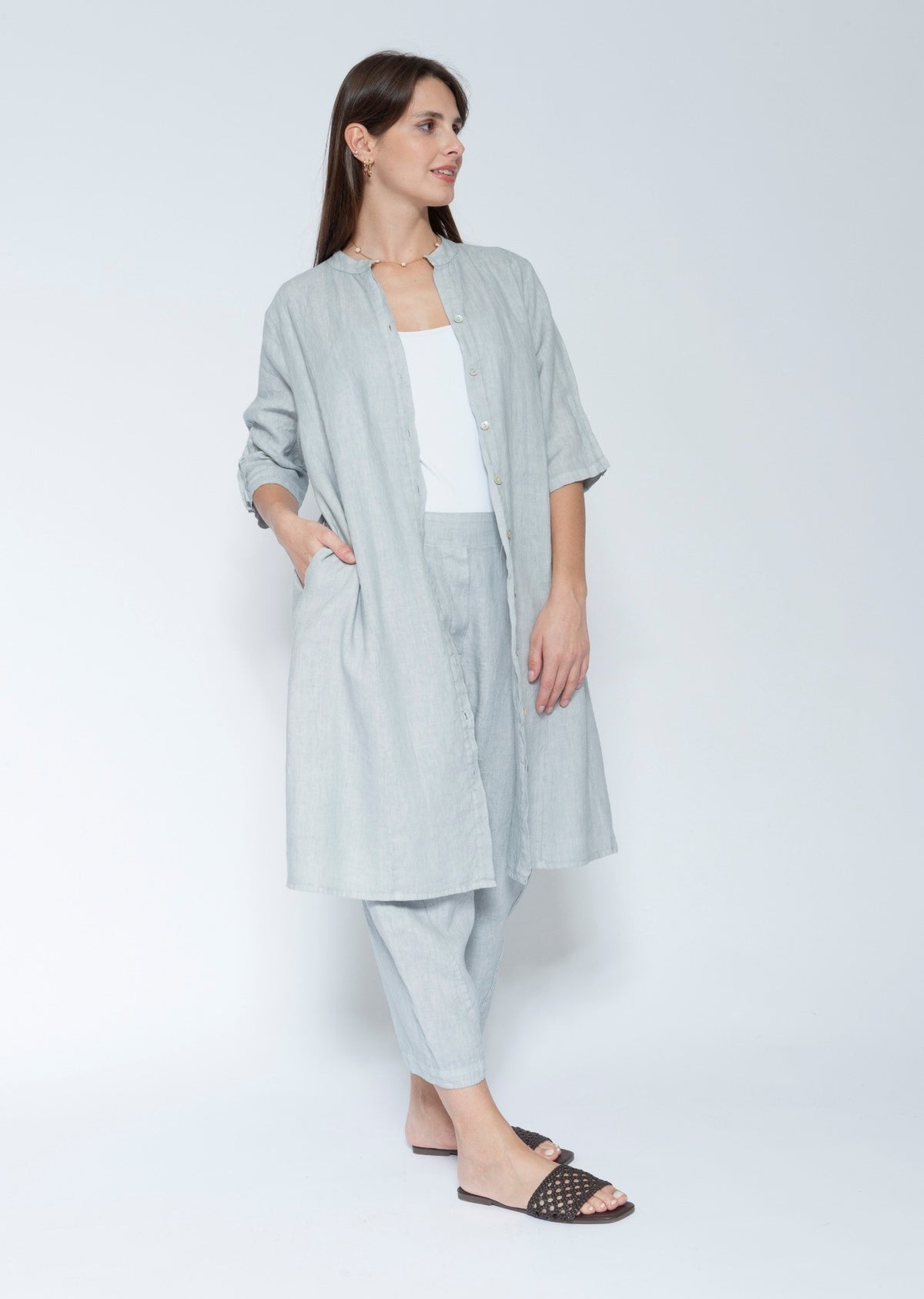 Front view light blue grey linen long shirt dress with matching trousers, worn over a white tank top and black slide sandals.