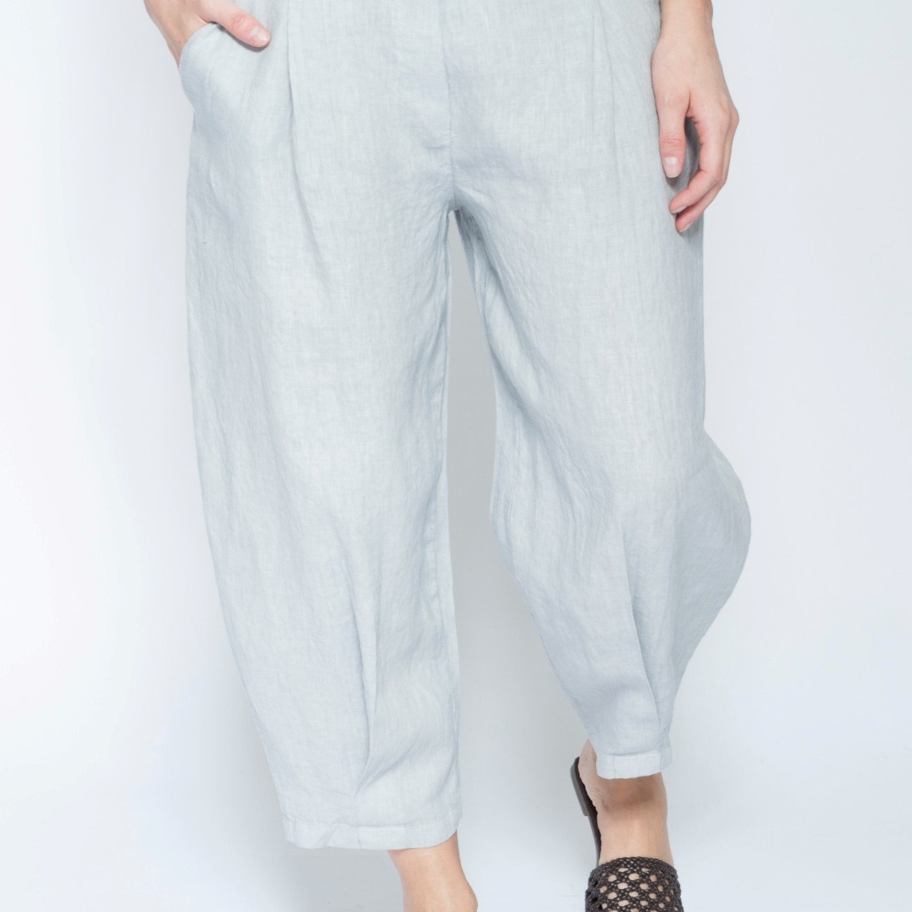 A person wearing light gray wide-leg cropped pants with side pockets, paired with black woven slide sandals, shown against a plain white studio background.