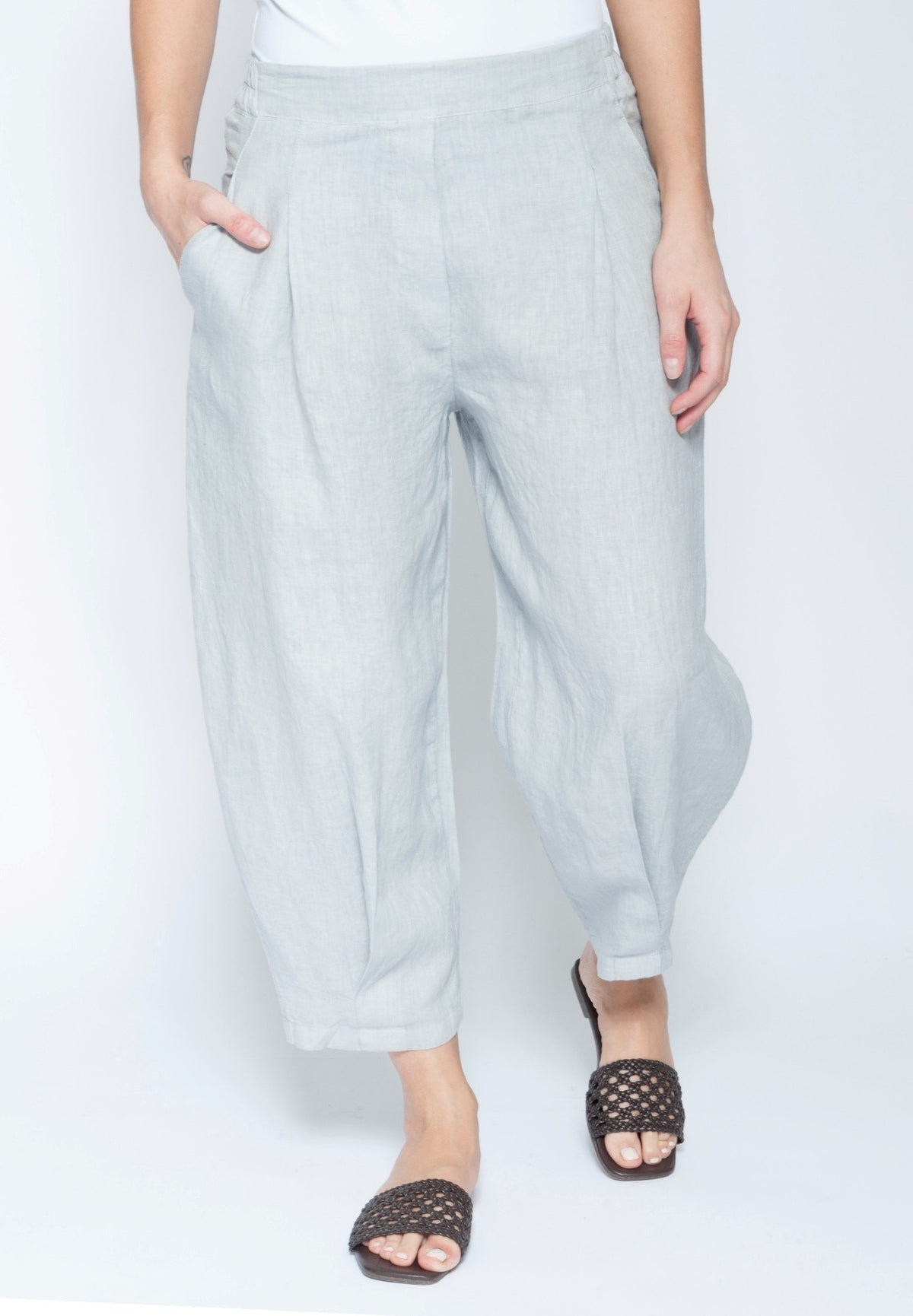 A person wearing light gray wide-leg cropped pants with side pockets, paired with black woven slide sandals, shown against a plain white studio background.