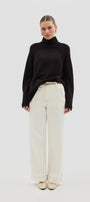 Woman wearing a black turtleneck sweater and white pants on a white background