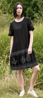 Woman wearing a black dress with embroidery in a grassy outdoor setting
