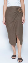 A model wearing a brown linen wrap midi skirt with a large round wooden button detail at the waist, paired with a white top and brown woven slide sandals, against a light gray background.