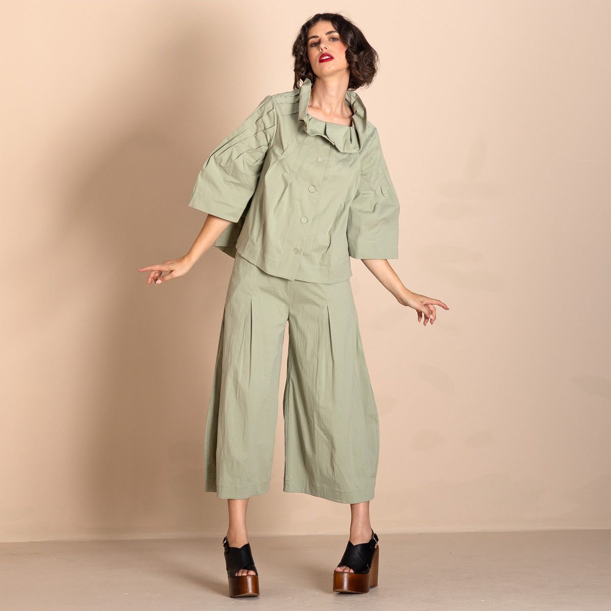  sage green two piece outfit consisting of a cropped, short sleeved button up top with pleated details and matching wide leg cropped pants, styled with black platform sandals.