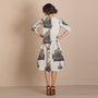 back view  wearing a knee length cream dress with a dark blue and beige architectural illustration print, paired with brown platform sandals.