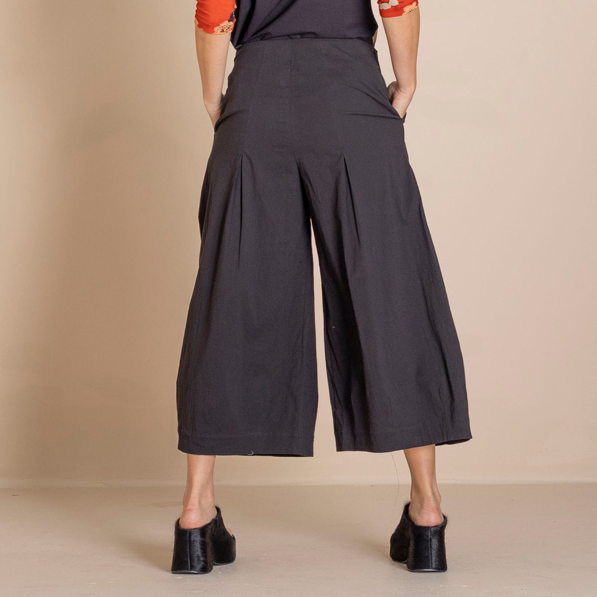 back  view  black wide leg cropped pants, a dark top with orange patterned sleeves, and black shoes.