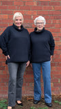 Two women wearing black sweaters and jeans standing against a brick wall.
