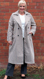 Woman wearing a checkered coat standing against a brick wall.
