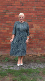 Woman wearing a patterned dress standing against a brick wall.