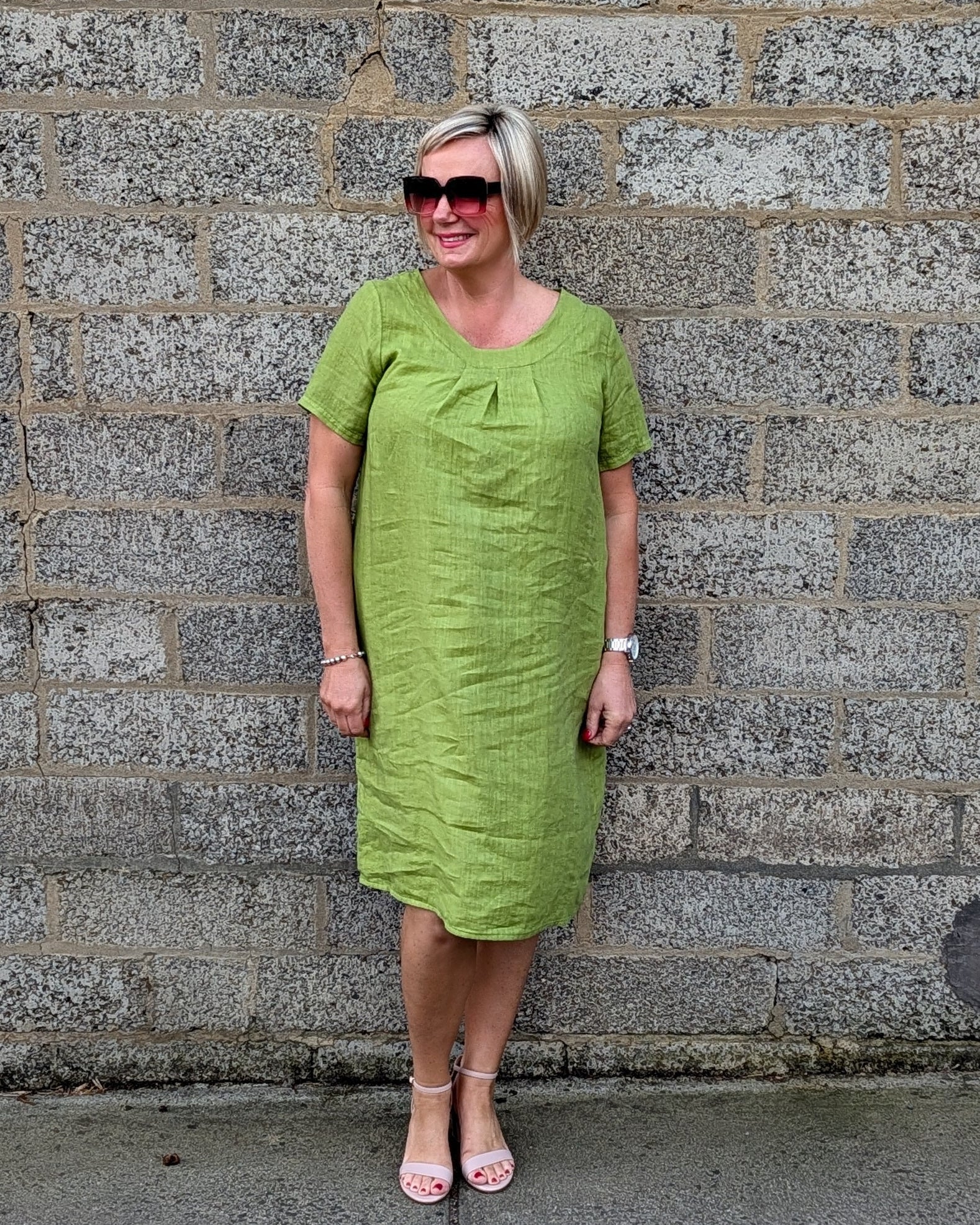 Front View lime green short sleeve midi dress, pink sunglasses, and pink sandals .