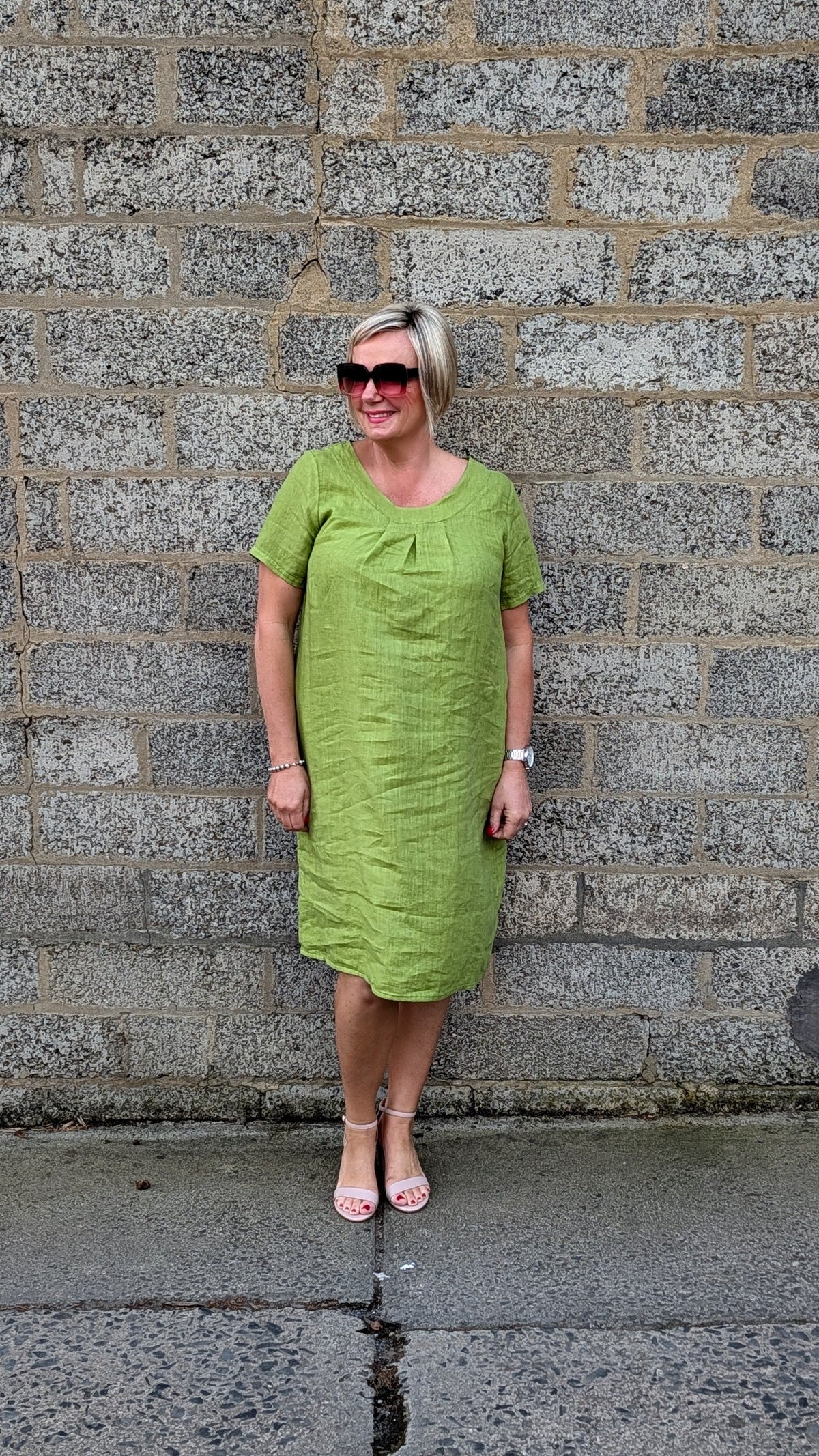 Front View lime green short sleeve midi dress, pink sunglasses, and pink sandals .